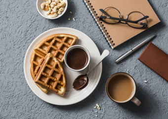 Coffee break in the workplace. Coffee and viennese waffles with chocolate sauce on a gray background, top view