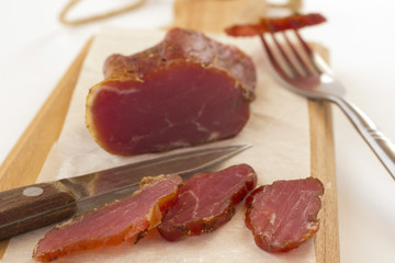 Sliced smoked meat on a cutting board. Slice of meat on fork and knife on white background