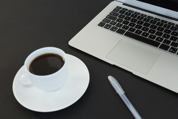 Obraz na płótnie Canvas Cup of coffee, laptop and pen on black background