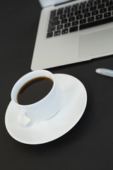 Cup of coffee, laptop and pen on black background