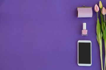 Tulips, purse, nail polish and mobile phone arranged on purple