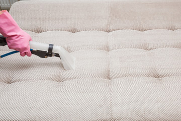 Dry cleaner's employee hand cleaning a sofa with professionally extraction method. Textile upholstered furniture. Early spring regular cleanup. Commercial cleaning company concept.