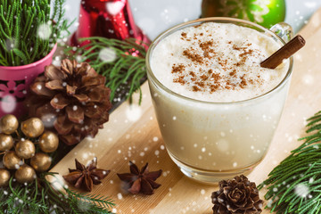 Eggnog, traditional drink for Christmas celebration party in glass topped with ground nutmeg and cinnamon stick, top view with copy space in Xmas theme decoration and snowfall effect background.
