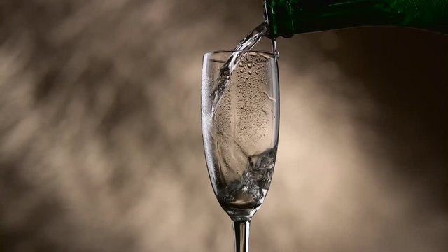 Glass is filled with champagne from a green bottle on a bokeh background