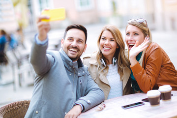 Group of three friends using phone in outdoor cafe on sunny day
