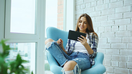 Young happy woman have online video chat using digital tablet computer sitting on balcony in modern...