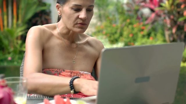 Attractive woman using modern ultrabook while relaxing in exotic place, steadycam shot

