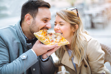 Couple eating pizza snack outdoors and smiling