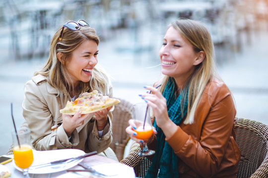 Portrait of two young women eating pizza outdoors having fun together.