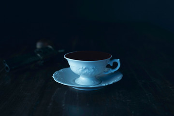 White tea cup filled with blood on wooden table with revolver.