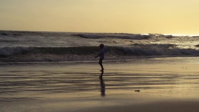 Boy walking on the beach next to the sea, steadycam shot, slow motion shot 

