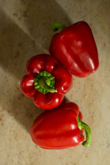 3 Red Peppers, Paprikas, Capsicums from above - neutral travertine background, side light