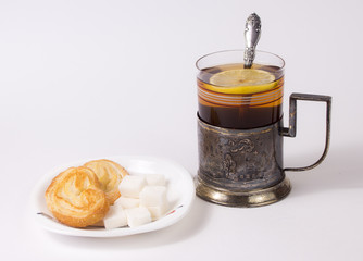 Glass with tea and teaspoon  in old silver glass-holder, sugar pieces  and cakes on white  background