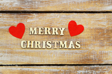 Merry Christmas written with wooden letters on rustic wooden surface with two red hearts
