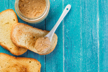  jar with peanut butter, spoon and toast on blue wooden table