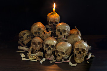 Pile of Skulls with candle and flame on the head and bone on black background in dark room
