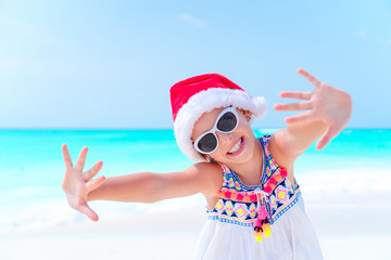 Obraz premium Happy little girl in Santa hat on Christmas beach vacation