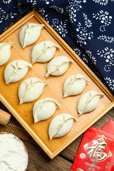 raw dumplings on wooden plate with flour and rolling pin and red packet,Chinese word translation:happiness