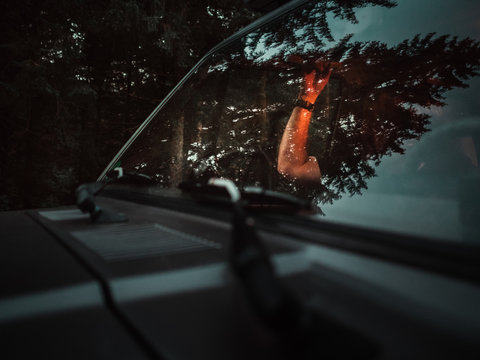 Hand im inneren eines Autos angeleuchtet von warmem Licht in der Umgebung eines Waldes 