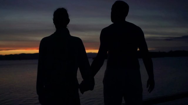 Couple holding each other hands and admires the sea at night, steadycam shot, slow motion shot at 240fps

