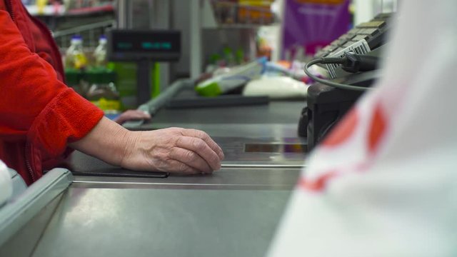 Close up check out counter. Senior female hands working on cash register in the supermarket