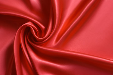 Close up of ripplesin shape of rose flower in red silk fabric. Satin textile background.