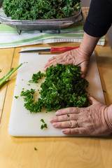 Hands of an older woman gathering freshly chopped kale on a white cutting board, vertical aspect