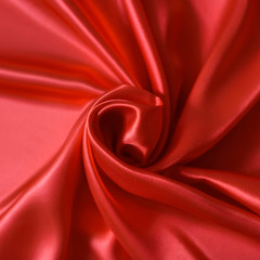 Close up of ripplesin shape of rose flower in red silk fabric. Satin textile background.