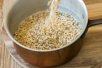 Pouring Whole Grain Brown Rice into Copper Pot Wood Table Motion Rustic Kitchen Interior Healthy Diet Fiber Source Mediterranean Cuisine Close Up