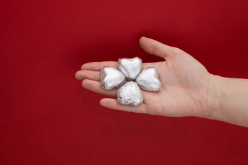 Chocolate heart shaped sweets in the foil laying on a females hand on red background. Beautiful love concept for Valentines day.