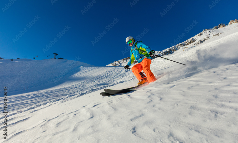 Wall mural Young skier running downhill in beautiful Alpine landscape.