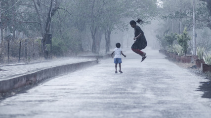 Mother and daughter welcoming the first monsoon showers by playing in heavy rain