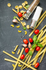 Concept of Italian cuisine. Pasta, spices, tomatoes and basil on a gray slate background. Flat lay, top view.