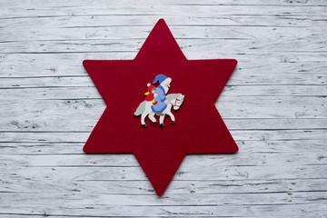 Weihnachtsmann in blauem Mantel und kleiner Engel auf weissem Pferd auf rotem Filzstern Hintergrund...