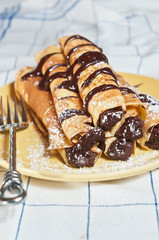 fresh, baked crepes filled with chocolate hazelnut ganache, sprinkled powder sugar on a yellow, round plate 