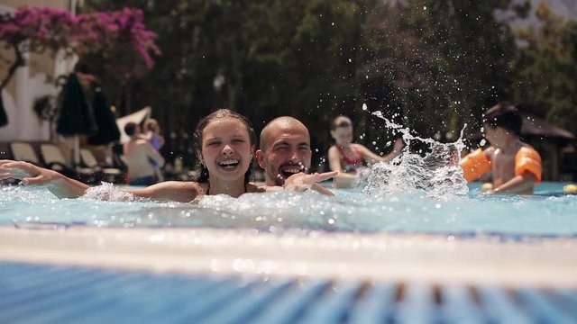 Young dad with a daughter playing and splashing in the pool