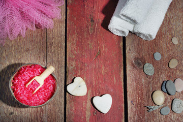 Spa set on a wooden red background, bath salt, loofah, white towels and stones in the form of hearts