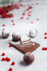 chocolate round candies, chocolate bars and red berries on a gray background and powdered sugar