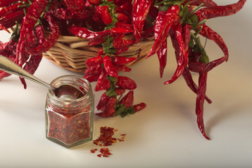 Peperoncino rosso piccante macinato nel vasetto di vetro, con peperoncini sani essiccati nel cesto. 