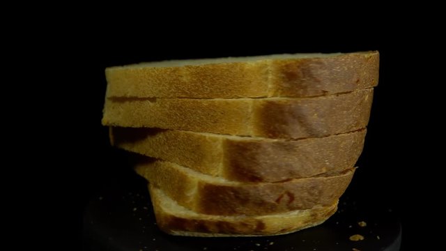 Close-up of sliced white wheat bread rotates against a black background, loopy motion.