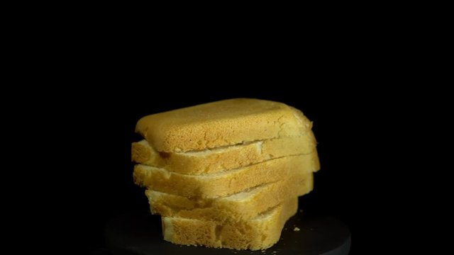 Close-up of sliced white wheat bread rotates against a black background, loopy motion.