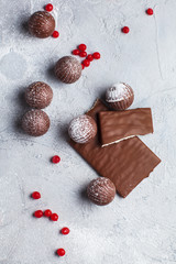 chocolate round candies, chocolate bars and red berries on a gray background and powdered sugar