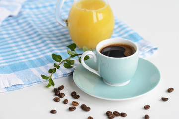 Strong black coffee in a light blue cup on a white table with orange juice