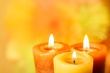 Three burning candles on a bright blurred background closeup