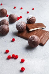chocolate round candies, chocolate bars and red berries on a gray background and powdered sugar