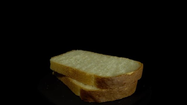 Close-up of sliced white wheat bread rotates against a black background, loopy motion.