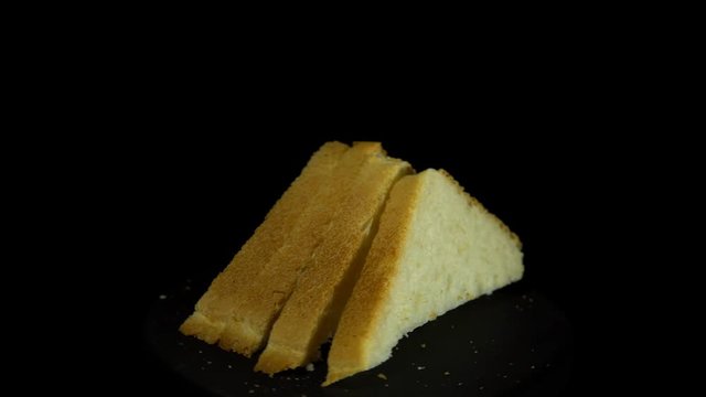 Close-up of sliced white wheat bread rotates against a black background, loopy motion.