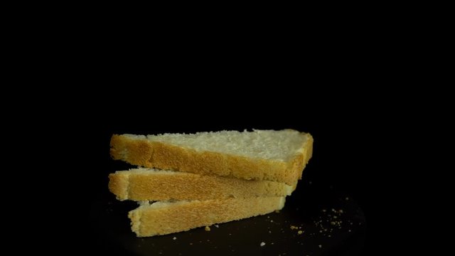 Close-up of sliced white wheat bread rotates against a black background, loopy motion.