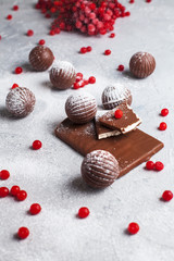 chocolate round candies, chocolate bars and red berries on a gray background and powdered sugar