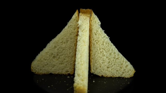 Close-up of sliced white wheat bread rotates against a black background, loopy motion.